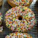 Colorful sprinkled vanilla doughnuts on a baking rack